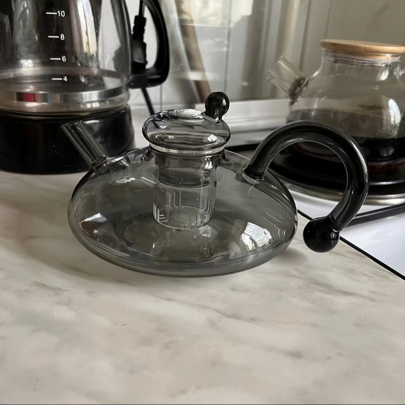 Elegant glass teapot with modern black handle on a kitchen counter.