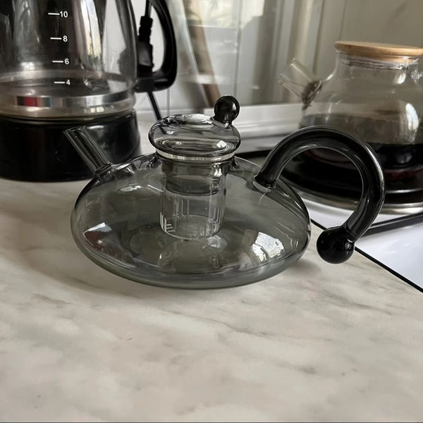 Elegant glass teapot with modern black handle on a kitchen counter.