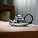 Elegant glass teapot with heat-resistant design and modern black handle on a wooden surface.