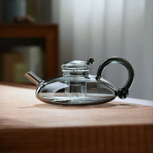 Elegant glass teapot with heat-resistant design and modern black handle on a wooden surface.