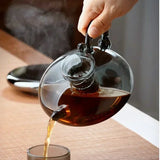 Elegant glass teapot pouring hot tea into a glass cup with a modern black handle.